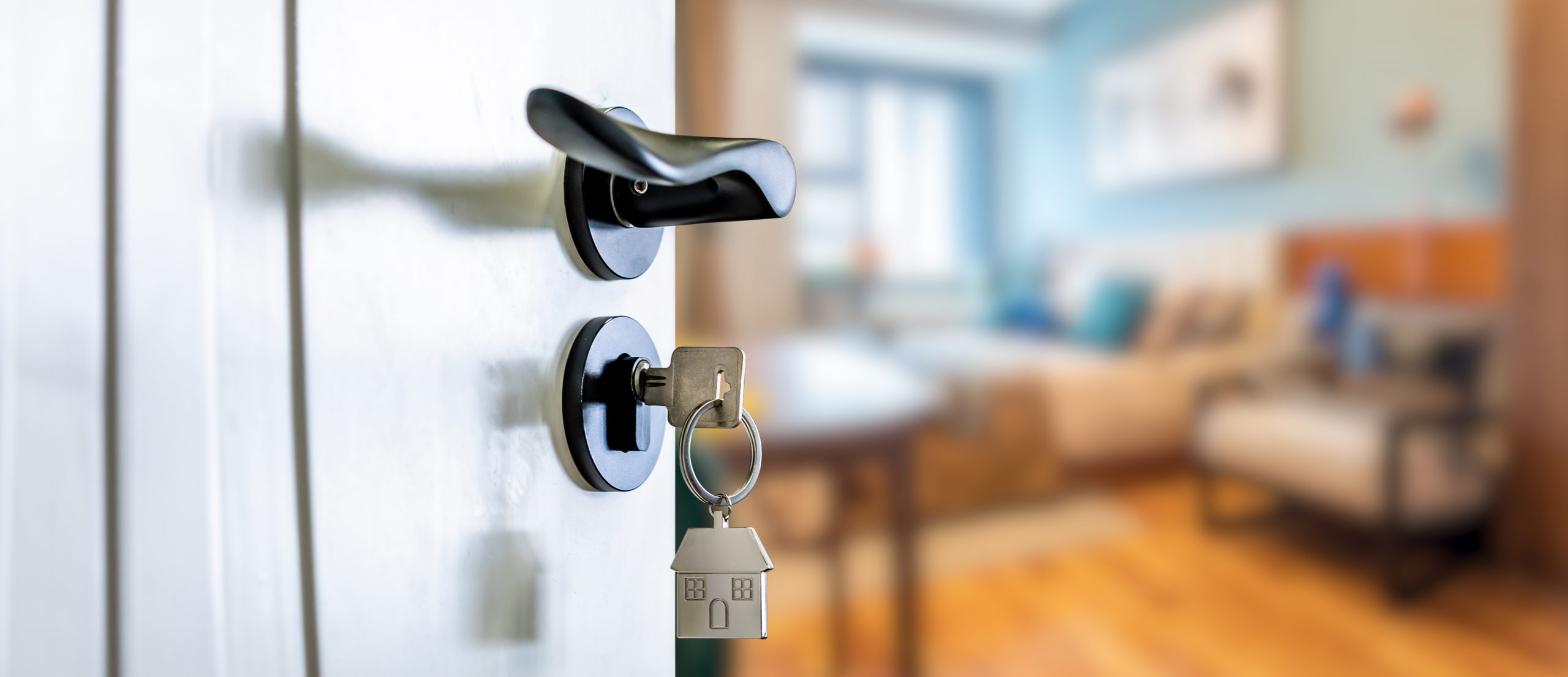 An open door with a key in the lock, a house pendant hanging from the key